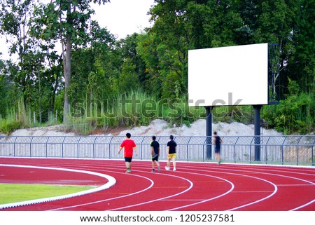 Selective focus picture at white broad in the football stadium with blurred picture of some people are jogging in the running track lanes