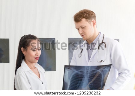 Medical professionals caucasian man holding xray and conversation with young woman Asia patient.Close up and copy space.