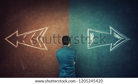 Puzzled businessman and a split blackboard with arrows going in two different ways red and blue side. Correct choice between left and right, failure or success. Difficult decision and doubt concept. Royalty-Free Stock Photo #1205245420