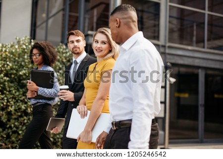Young businesswoman walking outside office with colleagues. Group of multi-ethnic business people waking outside office building.