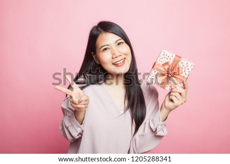 Asian woman show victory sign with a gift box on pink background