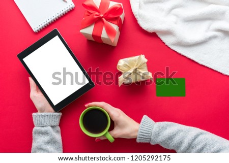Female hands, woman holding a tablet pc and Cup of coffee or tea. Business card, red table, gifts boxes for the holidays, background with copy space for advertisement, top view