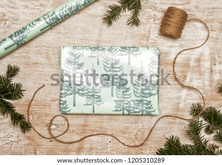 The process of packing a New Year and Christmas gift, a branch of spruce, twine, rope, green and pink paper on a wooden background. Top view, copy space, flat lay.