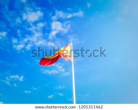 A huge Spanish flag waving in the wind against the blue sky with white clouds on a beautiful summer day in Madrid.