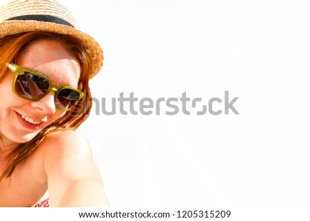 Young smiling red-haired woman in a straw hat and sunglasses photographing a selfie, isolated on white background.