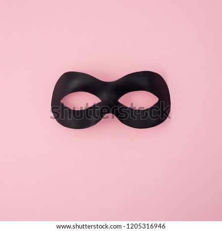 Black carnival mask on a light pink background.