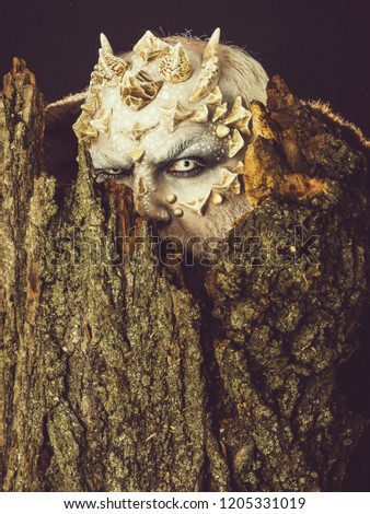 Tree spirit and fantasy concept. Goblin with horns on head. Man with dragon skin and bearded face. Druid behind old bark on black background. Monster with sharp thorns and warts.