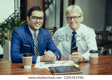 Two successful businessmen drinking coffee in office cafe and discussing ongoing project. Business partners reviewing financial report and calculating profit . Business meeting and success concept