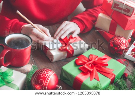 Female Hand writing greeting card with red and brown gift boxes for Christmas and New year. 