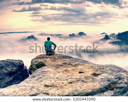 Photographer down on knees takes photos with mirror camera on exposed rock. Tourist using tripod to take pictures of misty fall landscape