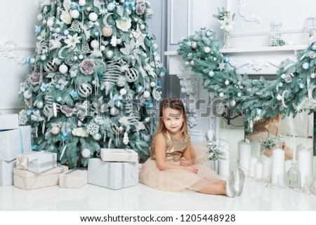 Little girl posing near the Christmas tree in the room.