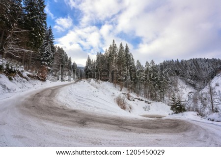 Narrow winding mountain road, alpine winter landscape with trees and blue cloudy sky