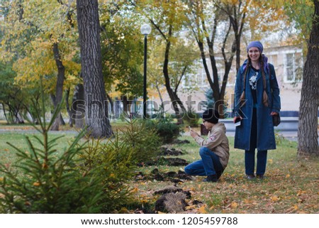 A woman and her child taking pictures on a mobile phone of a small tree in the Park in the fall.