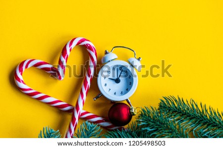 christmas alarm clock  and lolipop on yellow background