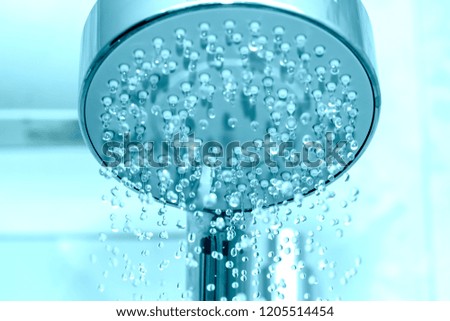 Closeup of a shower head with sprinkling water, blue toned photo.