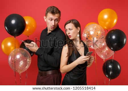 Couple stand back to back messaging in cellphone celebrating birthday holiday party isolated on red background air balloons. St. Valentine International Women Day Happy New Year 2019 concept. Mock up