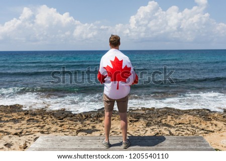 A man stands on the pier and admires the sea covered with a Canadian flag with a picture of a maple. Travel and tourism. Patriotic happy mood.