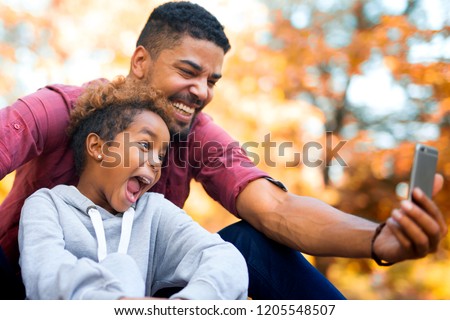 Father and daughter taking selfie with smartphone while making funny faces. Laughter and happiness all around. 