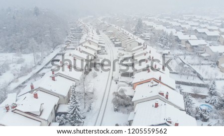 AERIAL: Flying over the empty road leading through the vast suburbs covered in the fresh fallen snow. Fairytale shot from the air of a blizzard covering the houses in the powder snow. Idyllic winter