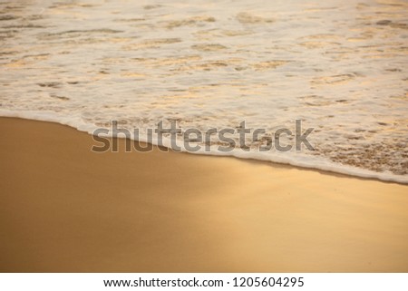 A close up of the waters edge at a beach with golden sand and the white bubbling foam of the ocean.