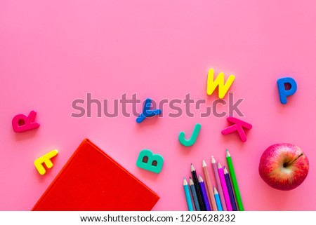 Primary school concept. Letters of english alphabet, book, apple and color pencils on pink background top view copy space