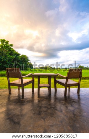 Two wooden chairs on lush green lawn with view of countryside and orange sky