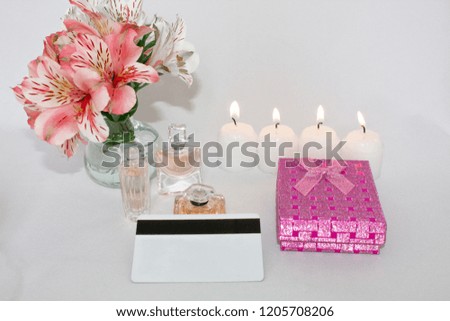 Picture of a pink luxury gift box with a bouquet of beautiful Alstroemeria flowers, a romantic candle, perfume and a credit card. Dressing table with women's accessories.