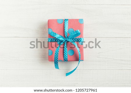 A gift wrapped in pink paper in a blue circle and ribbon, on a white wooden table.