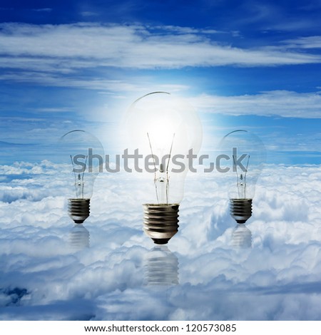 clear electric light bulb glowing against blue sky and cloud background