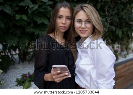 Two young women are standing on the street and using a smartphone.