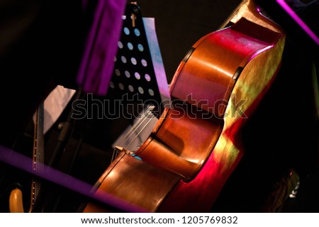 Wooden cello or violin on stage prepared for playing. Music sheets and notes on stand. Classical instruments. Concept of orchestra music. Audience waiting for concert to begin
