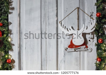 wooden toy moose elk skates in a Santa Claus costume hanging on a wall surrounded by fir and rowan tree branches