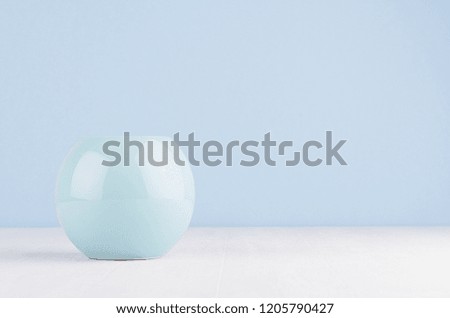 Glossy light blue ceramic sphere on white wood board and soft blue wall. Elegant simplicity in home decoration.