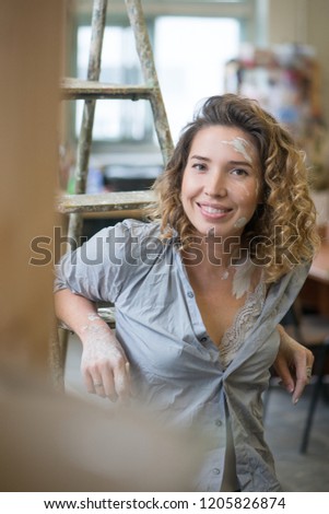 Beautiful young girl sitting in the workplace in a creative workshop smiling and dreaming. She smeared with clay
