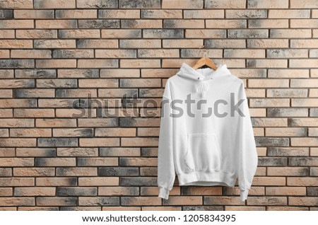 New hoodie sweater with hanger on brick wall. Mockup for design