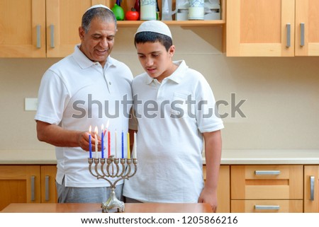Happy family is lighting a candle celebrating together Jewish holiday Hanukkah. Jewish Dad and teenager son or grandfather with grandson lighting Chanukkah Candles in a menorah for the holdiay