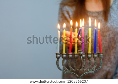 Jewish Woman lighting Hanukkah Candles in a menorah. People celebrate Chanukah by lighting candles on a menorah, also called a Hanukiyah. Each night, one more candle is lit.