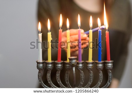 Jewish Woman lighting Hanukkah Candles in a menorah. People celebrate Chanukah by lighting candles on a menorah, also called a Hanukiyah. Each night, one more candle is lit.