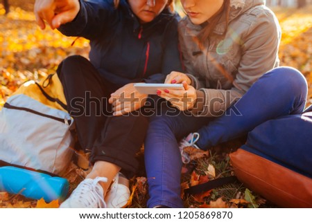 Couple of tourists with backpacks searching for right way using navigator on phone in autumn forest. Women having rest
