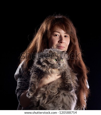 Young beautiful smiling woman holds fluffy cat, on black background