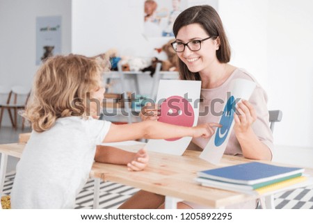 Smiling counselor holding pictures during meeting with young patient with autism