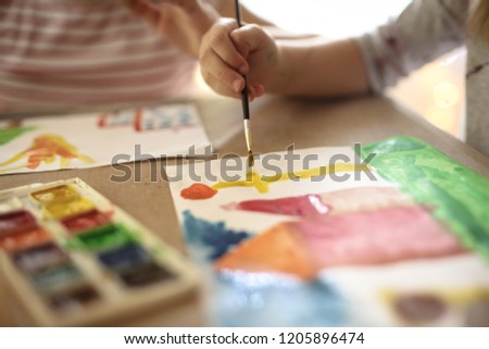 child draws with a brush and paints on a sheet of paper, lifestyle and blurred background, the concept of child development and creativity