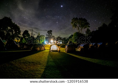 View of night sky with stars, with tents in camping field with illumination with light. Travel, outdoor and nature.