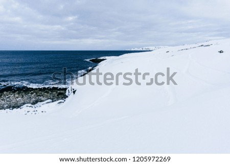 rocky coast of blue cold ocean in the north covered with snow in a winter frosty day