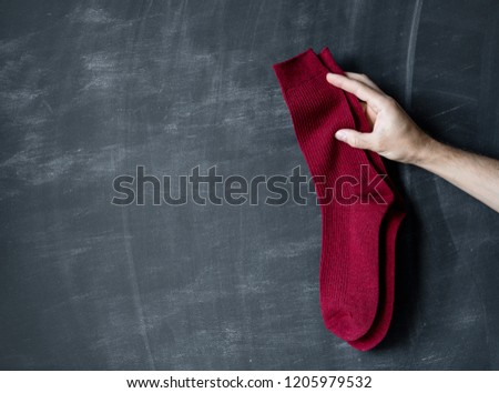 Warm red socks in the hand of a man against the background of a dark board.