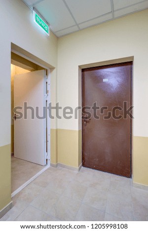 Illuminated corridor in modern  residential building with iron doors fire alarm on wall and with an emergency exit sign on the wall