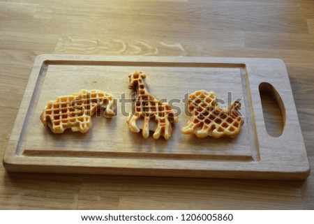 Three homemade waffles in animal shapes on the wooden board and wooden background 