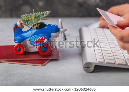 Small airplane with christmas tree, passports, keyboard, credit card on grey background. Vacation, tourism, travel for christmas. Woman hands booking tickets online for Christmas eve.