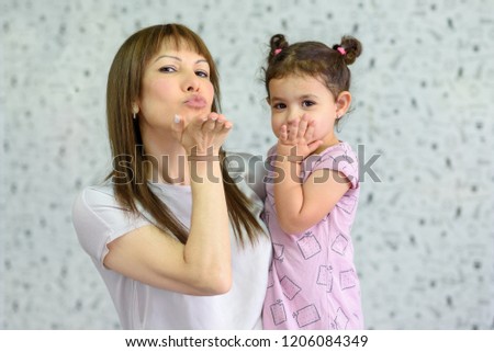 Lovely family. Little happy girl and her mom smiling cheerfully and sending air kiss. Happy senior woman young grandma hugging her beautiful grandchild and sending air kiss.