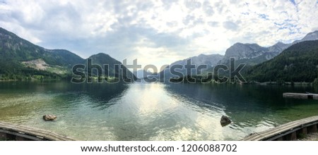 Panoramic view over Austrian mountains with graceful lake in between the landmarks. The lake has a beautiful reflective mirror view image of the sky which makes the picture even more interesting.